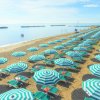 Una spiaggia con file di ombrelloni verdi e bianchi.