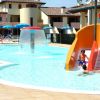 Piscina con scivolo arancione, giochi d'acqua e ombrelloni blu.