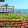 Un terrazzo con tavolini e sedie vista mare, ombrelloni di paglia e aiuole fiorite.