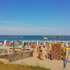 Spiaggia affollata, persone in costume, ombrelloni blu e giochi per bambini vicino al mare.
