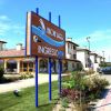 Cartello d'ingresso di un resort con edifici e auto parcheggiate.