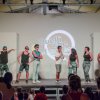 Sei persone su un palco partecipano a uno spettacolo con un pubblico seduto che li osserva.