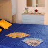 Camera da letto con copriletto blu, cuscini gialli e volantini sparsi su una superficie liscia.