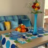 Tavolo apparecchiato con piatti blu, frutta, e vaso di fiori. Divano blu a quadri sullo sfondo.