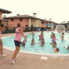 Persone si divertono in piscina, insieme a due animatrici con magliette rosa.
