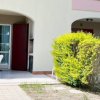 Patio esterno con tavolo bianco e sedie, circondato da siepi e piante verdi.