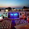 Un cortile all'aperto con palco illuminato e sedie bianche, durante il tramonto.