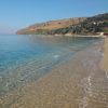 Spiaggia sabbiosa con acqua limpida e colline sullo sfondo.