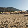 Spiaggia con ombrelloni gialli, colline sullo sfondo.