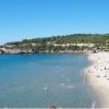Spiaggia sabbiosa con bagnanti, mare calmo, una torre in lontananza e collina verde.