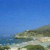 Spiaggia affollata con ombrelloni colorati, colline sullo sfondo.