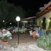 Cena all'aperto con persone sedute a tavoli sotto luci e accanto ad un edicola gialla.