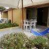 Piccolo patio con sedie bianche e una sdraio blu, protetto da grandi ombrelloni.