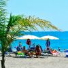 Una spiaggia con ombrelloni bianchi, sdraio blu e persone che si godono il sole.