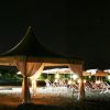 Una spiaggia di notte con un gazebo illuminato e sedie a sdraio disposte ordinatamente.