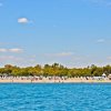 Spiaggia affollata vista dal mare, ombrelloni e vegetazione sullo sfondo.