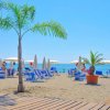 Spiaggia con lettini blu e ombrelloni bianchi, palme in primo piano.