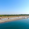 Spiaggia con ombrelloni bianchi e vele sul mare in una giornata soleggiata.