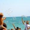 Un bambino seduto su una spalla gioca con bolle di sapone sulla spiaggia.