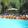 Un gruppo di persone con magliette arancioni sedute a bordo piscina, spruzzando acqua.