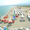 Spiaggia con vele colorate e file di ombrelloni bianchi.