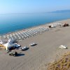 Spiaggia con file di ombrelloni e barche a vela.