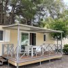Casa mobile con veranda coperta, tavolo e sedie in un ambiente boschivo.
