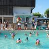 Bambini nuotano in piscina, adulti animano a bordo.