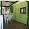 Veranda in legno di una casa mobile verde, tavolo e sedie bianche.