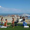 Persone su una spiaggia, alcune sotto un ombrellone. Il mare si estende all'orizzonte.