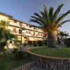 Edificio a tre piani con palme e giardino curato davanti.