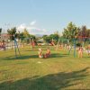 Un parco giochi con altalene su un prato verde. Bambini giocano e si divertono al sole.