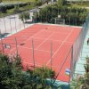 Un campo sportivo con superficie rossa, circondato da recinzioni e vegetazione.