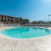 Piscina a forma ovale con lettini disposti intorno, edifici sullo sfondo.