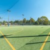 Campo sportivo all'aperto con erba sintetica e reti, circondato da recinzioni.