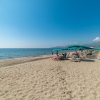 Spiaggia sabbiosa con lettini e ombrelloni verdi, mare calmo a sinistra.