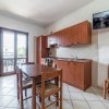 Cucina con mobili in legno, tavolo con sedie, TV appesa e porta finestra.