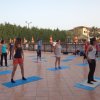 Persone fanno yoga su tappetini all'aperto su una terrazza soleggiata.