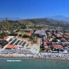 Vista aerea di una spiaggia frequentata, con edifici residenziali e una collina con un'antica torre.
