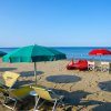 Spiaggia sabbiosa con ombrelloni verdi, lettini gialli e canoe rosse vicino al mare calmo.