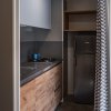 Cucina compatta con mobili in legno, frigorifero grigio e tendina a righe bianche e grigie.
