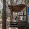 Una casa mobile tra gli alberi con una veranda in legno e sedie.