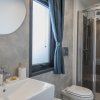 Bagno con lavandino bianco, doccia con porta in vetro e finestra.