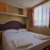 Camera con letto matrimoniale, testiera colorata, finestre con tende arancioni e bianche.