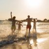 Persone che corrono in riva al mare al tramonto.