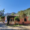Casa rosa tra gli alberi con montagne sullo sfondo.