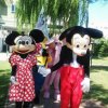 Personaggi in costume, simili a topi famosi, passeggiano in un giardino.