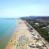 Spiaggia lunga con ombrelloni colorati, mare calmo a sinistra, città e colline in lontananza.