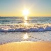 Tramonto sul mare con onde che si infrangono su sabbia dorata.