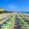Spiaggia con file di ombrelloni giallo-verdi, mare sullo sfondo e un hotel a sinistra.